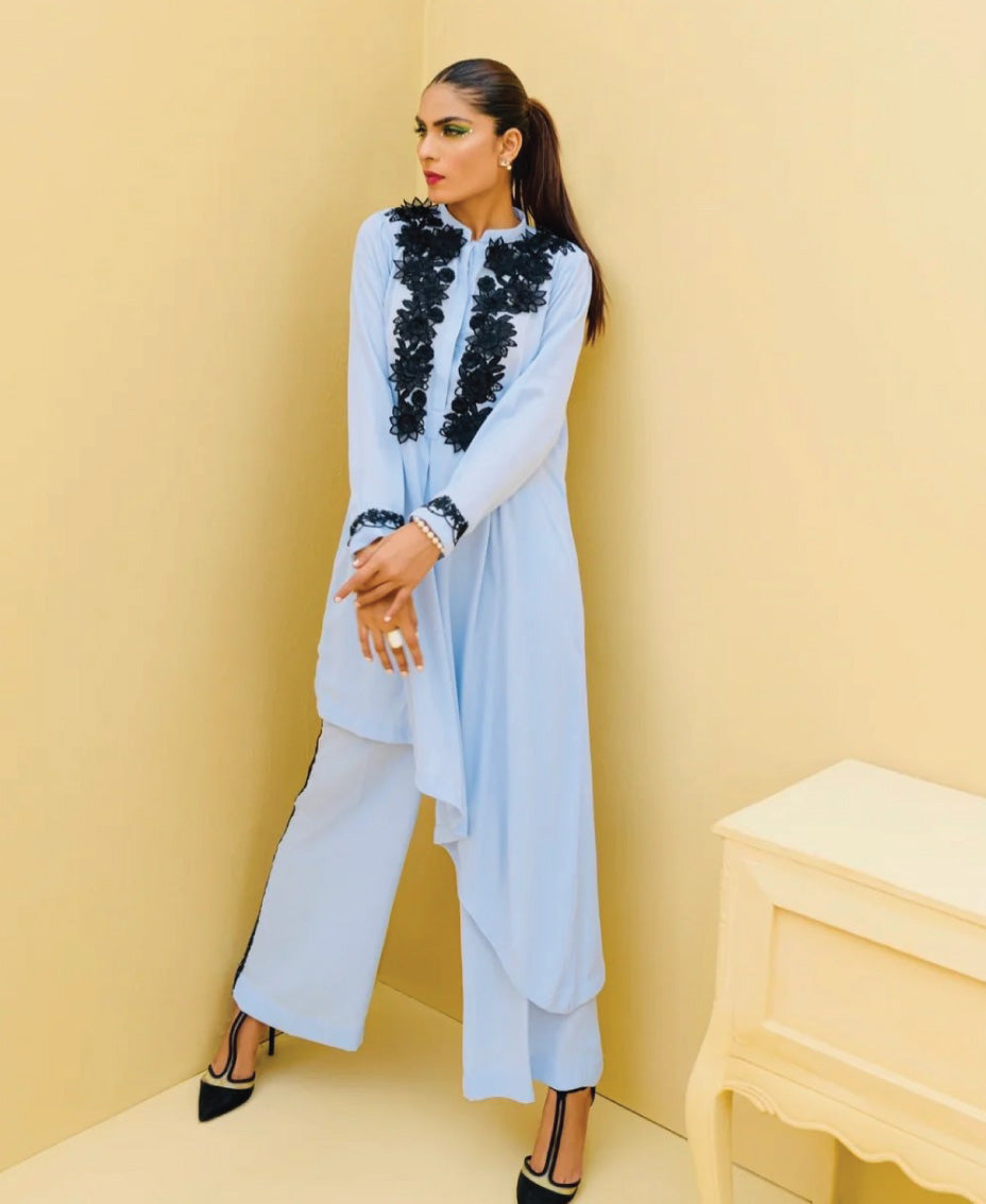 A woman standing against a yellow background, wearing a blue 2-piece co-ord set with black detailing on the top and bottom.