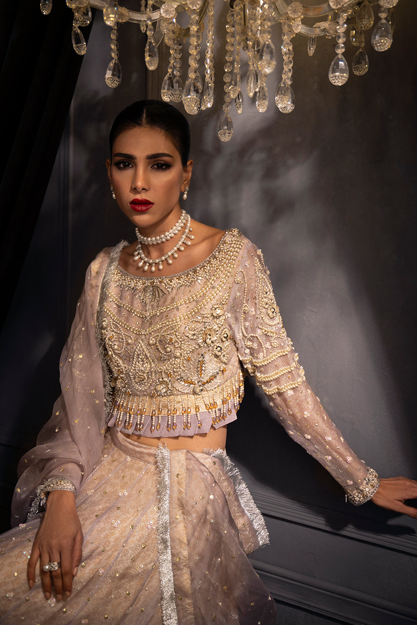 Lilac Lumière artisanal designer ensemble features an opulently embellished lilac blouse with pearl and crystal accents, styled with a fluid shimmer organza lehenga for elevated couture elegance.