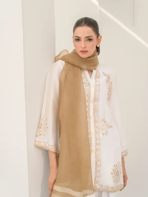 Woman wearing a beige and white embroidered outfit .