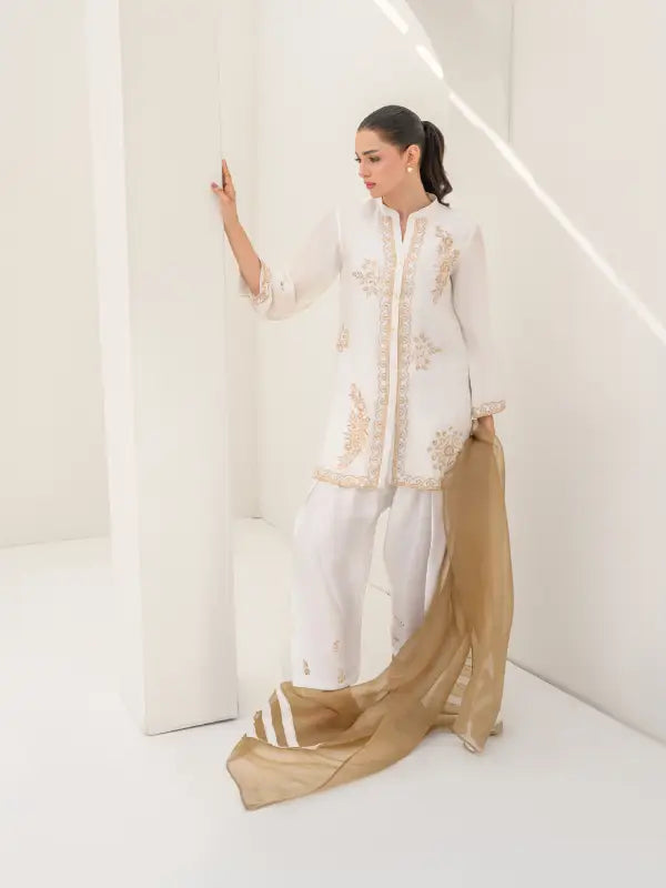 A white ivory embroidered three-piece set for women with gold detailing on shirt and on the shalwar and soft beige dupatta.


